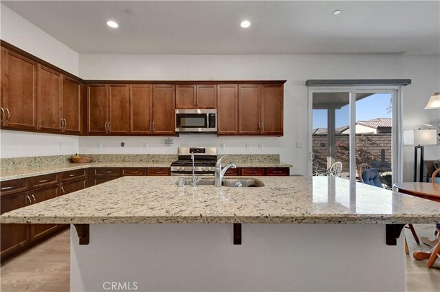 kitchen featuring appliances with stainless steel finishes, a kitchen breakfast bar, sink, a kitchen island with sink, and light stone counters