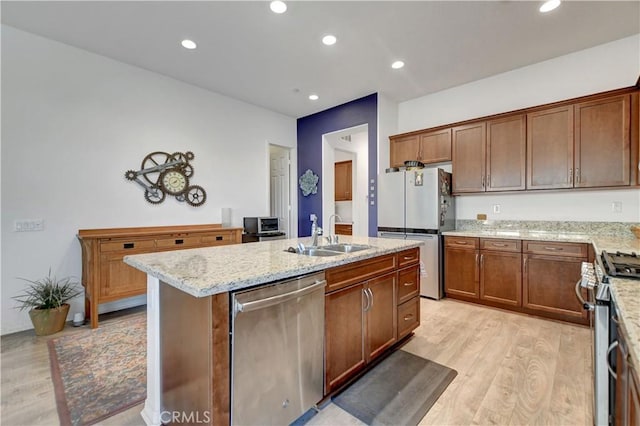 kitchen with a center island with sink, sink, light wood-type flooring, light stone countertops, and stainless steel appliances