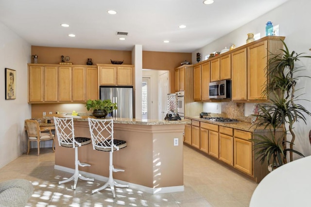 kitchen with backsplash, light stone countertops, appliances with stainless steel finishes, a kitchen island, and a breakfast bar area