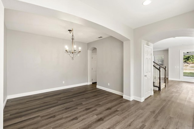 empty room with dark wood-type flooring and a notable chandelier