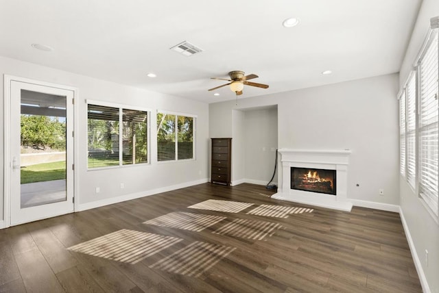 unfurnished living room featuring ceiling fan, a healthy amount of sunlight, and dark wood-type flooring