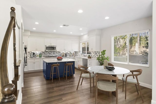 kitchen with decorative backsplash, appliances with stainless steel finishes, a center island, dark hardwood / wood-style floors, and white cabinetry