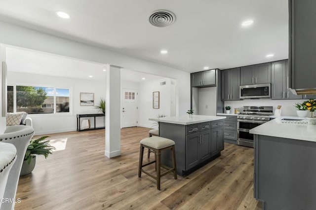 kitchen with a center island, dark wood-type flooring, a breakfast bar area, gray cabinets, and stainless steel appliances