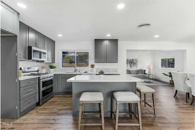 kitchen with a kitchen bar, wood-type flooring, stainless steel appliances, and gray cabinetry