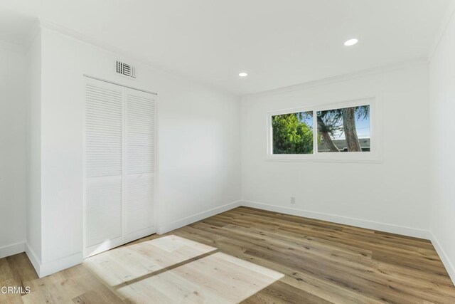 unfurnished bedroom featuring hardwood / wood-style flooring, ornamental molding, and a closet