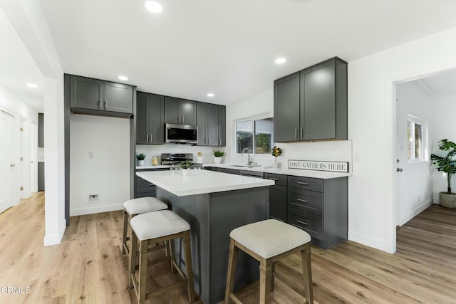 kitchen featuring gray cabinetry, sink, stainless steel appliances, a kitchen island, and light wood-type flooring