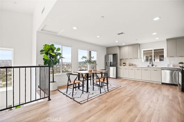 kitchen with gray cabinetry, sink, backsplash, appliances with stainless steel finishes, and light wood-type flooring