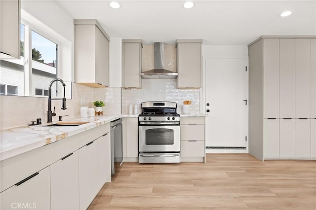 kitchen featuring sink, stainless steel appliances, wall chimney range hood, backsplash, and light hardwood / wood-style floors