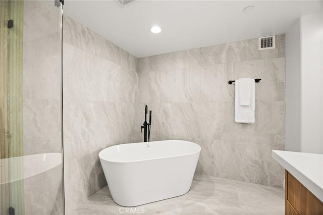 bathroom featuring a washtub, vanity, and tile walls