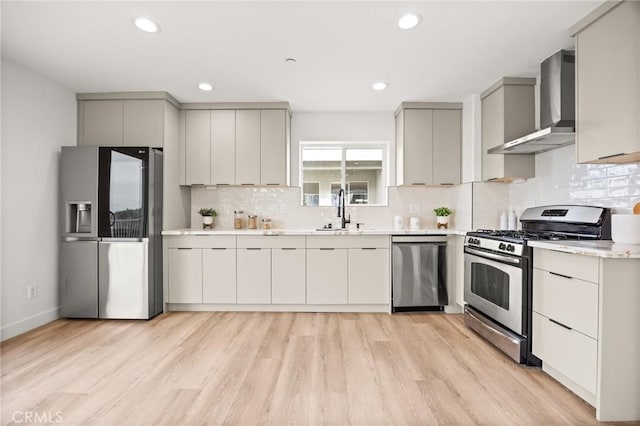 kitchen with sink, wall chimney exhaust hood, stainless steel appliances, decorative backsplash, and light wood-type flooring