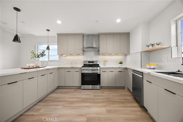 kitchen with stainless steel appliances, hanging light fixtures, gray cabinetry, and wall chimney range hood