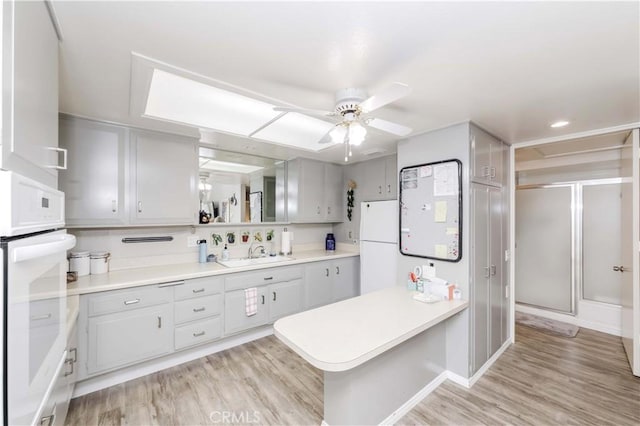 kitchen with ceiling fan, sink, kitchen peninsula, light hardwood / wood-style floors, and white appliances