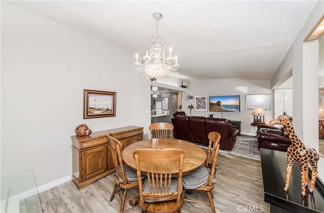 dining space featuring vaulted ceiling, light wood-type flooring, a textured ceiling, and a chandelier