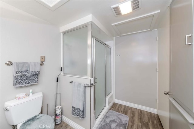 bathroom with hardwood / wood-style floors, toilet, and a shower with door