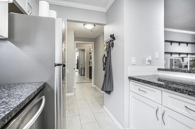 kitchen featuring white cabinetry, dark stone countertops, stainless steel refrigerator, light tile patterned floors, and crown molding