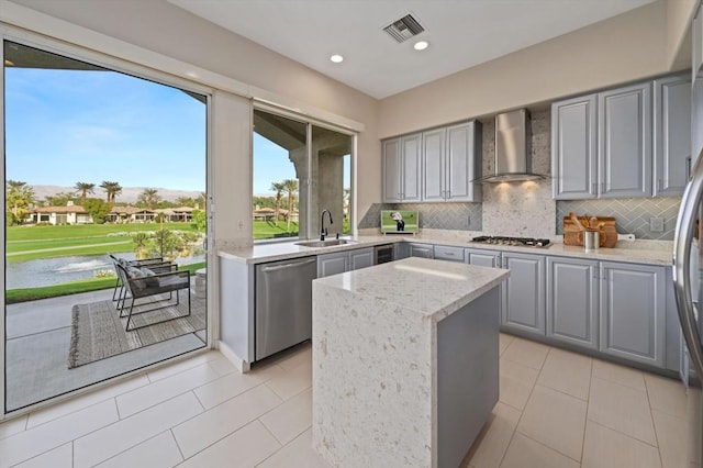 kitchen featuring wall chimney exhaust hood, sink, light stone counters, appliances with stainless steel finishes, and decorative backsplash