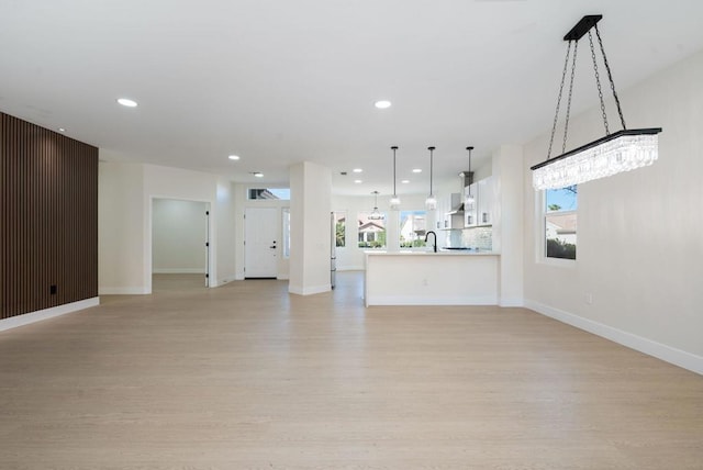 unfurnished living room with light hardwood / wood-style floors, sink, and a chandelier