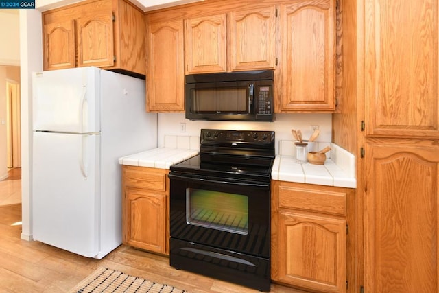 kitchen featuring tile counters, light hardwood / wood-style floors, and black appliances