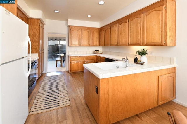 kitchen with tile countertops, light hardwood / wood-style floors, kitchen peninsula, sink, and white refrigerator