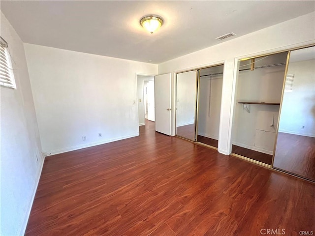 unfurnished bedroom with dark hardwood / wood-style floors and two closets