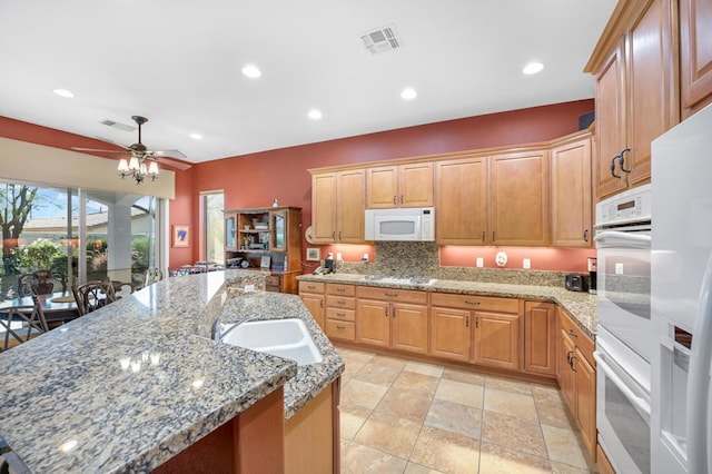 kitchen featuring ceiling fan, a center island with sink, light stone counters, and white appliances