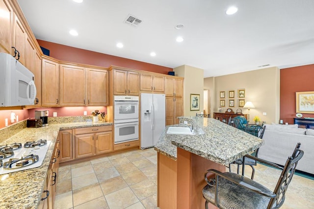 kitchen with white appliances, a kitchen island, light stone counters, a breakfast bar, and sink