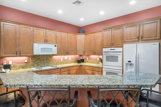 kitchen featuring kitchen peninsula, light stone counters, a kitchen breakfast bar, and white appliances