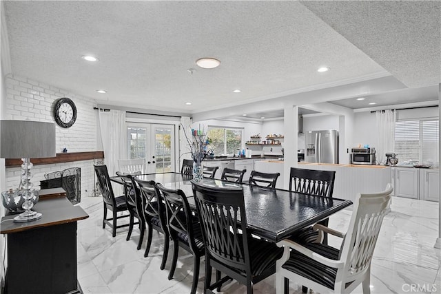 dining space featuring french doors, crown molding, a fireplace, a textured ceiling, and brick wall