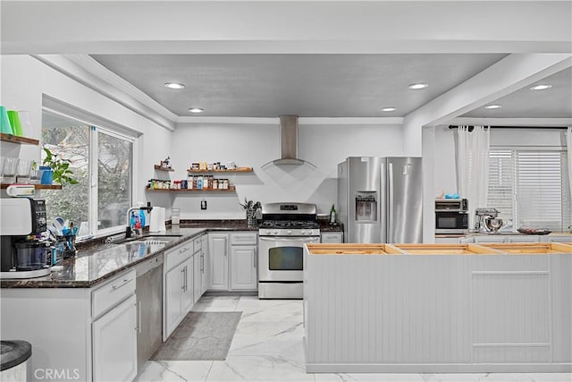 kitchen featuring appliances with stainless steel finishes, sink, wall chimney range hood, dark stone countertops, and white cabinetry