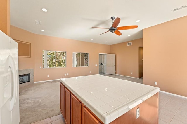 kitchen featuring tile counters, ceiling fan, white refrigerator with ice dispenser, and light carpet