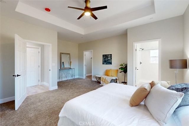 bedroom with a tray ceiling, ensuite bath, light carpet, and ceiling fan