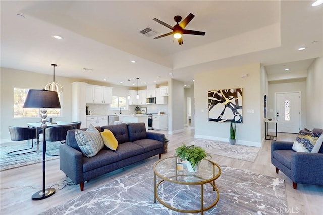 living room with a raised ceiling, light hardwood / wood-style floors, plenty of natural light, and ceiling fan