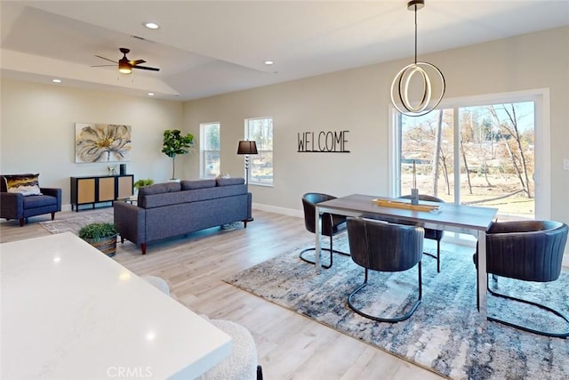 interior space with a raised ceiling, ceiling fan, and light hardwood / wood-style floors