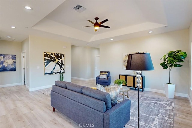 living room with light wood-type flooring, a tray ceiling, and ceiling fan