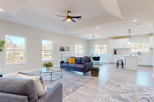 living room featuring light hardwood / wood-style floors, a raised ceiling, ceiling fan, and sink