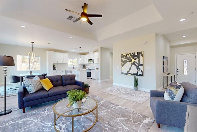 living room featuring light wood-type flooring, a raised ceiling, and ceiling fan