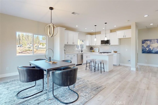 dining area with sink, light hardwood / wood-style flooring, a healthy amount of sunlight, and a notable chandelier