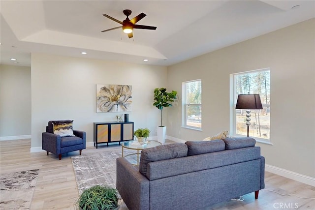 living room featuring light hardwood / wood-style floors, a raised ceiling, and ceiling fan