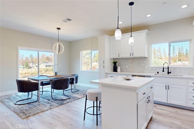 kitchen featuring sink, a center island, light hardwood / wood-style floors, white cabinetry, and hanging light fixtures