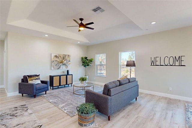 living room featuring a tray ceiling, ceiling fan, and light hardwood / wood-style floors