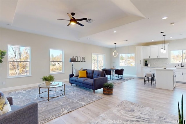 living room featuring ceiling fan, light wood-type flooring, sink, and a tray ceiling