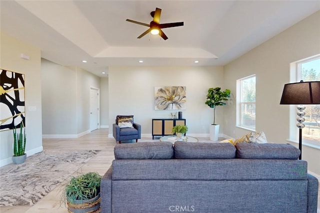 living room with a raised ceiling, ceiling fan, and light hardwood / wood-style floors