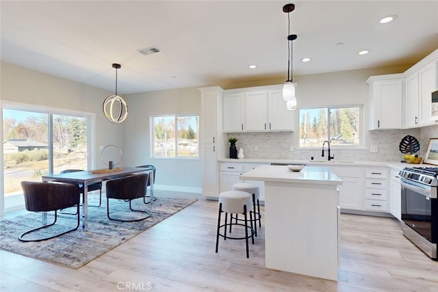 kitchen with white cabinetry, stainless steel range, sink, light hardwood / wood-style flooring, and a kitchen island