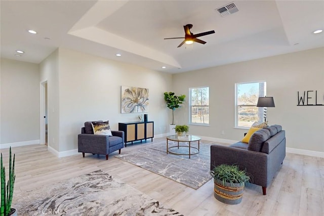 living room with a tray ceiling, light hardwood / wood-style flooring, and ceiling fan