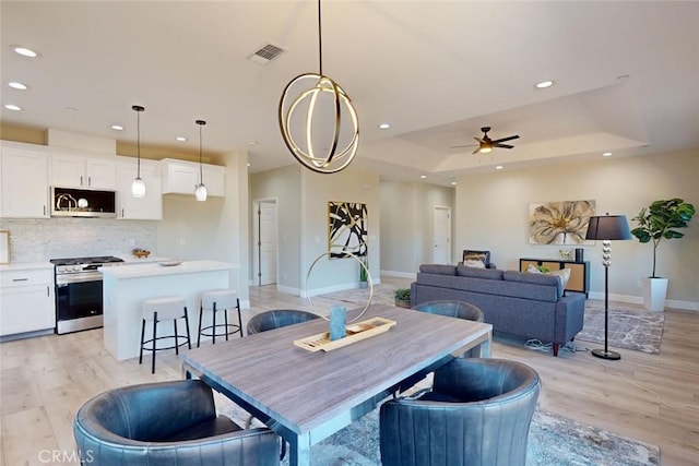 dining space with ceiling fan with notable chandelier, light hardwood / wood-style floors, and a raised ceiling