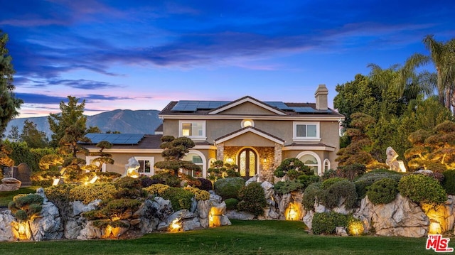 front facade featuring a lawn, a mountain view, and solar panels