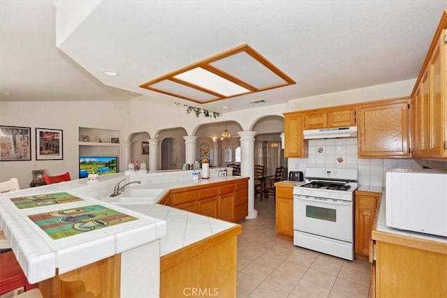 kitchen featuring gas range gas stove, sink, kitchen peninsula, vaulted ceiling, and light tile patterned floors