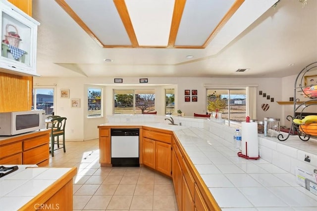 kitchen with white appliances, a tray ceiling, tile counters, and light tile patterned flooring