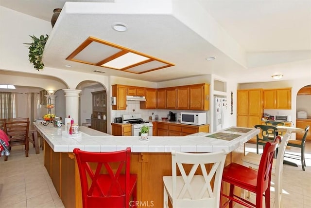 kitchen featuring tile countertops, a kitchen breakfast bar, white appliances, and light tile patterned floors