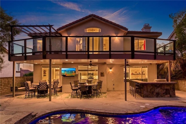 back house at dusk with ceiling fan, a patio, and a bar